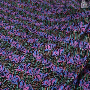 May include: Black fabric with a repeating pattern of pink and blue stylised flowers on green stems. The fabric has a slight sheen.