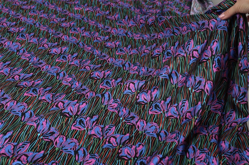 May include: Black fabric with a repeating pattern of pink and blue stylised flowers on green stems. The fabric has a slight sheen.
