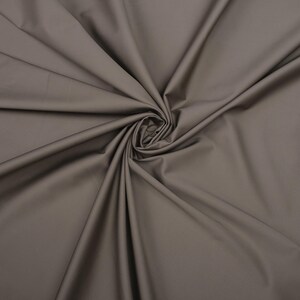 May include: A close-up of a smooth, gray fabric with a soft, drapey texture. The fabric is folded and arranged in a swirling pattern.