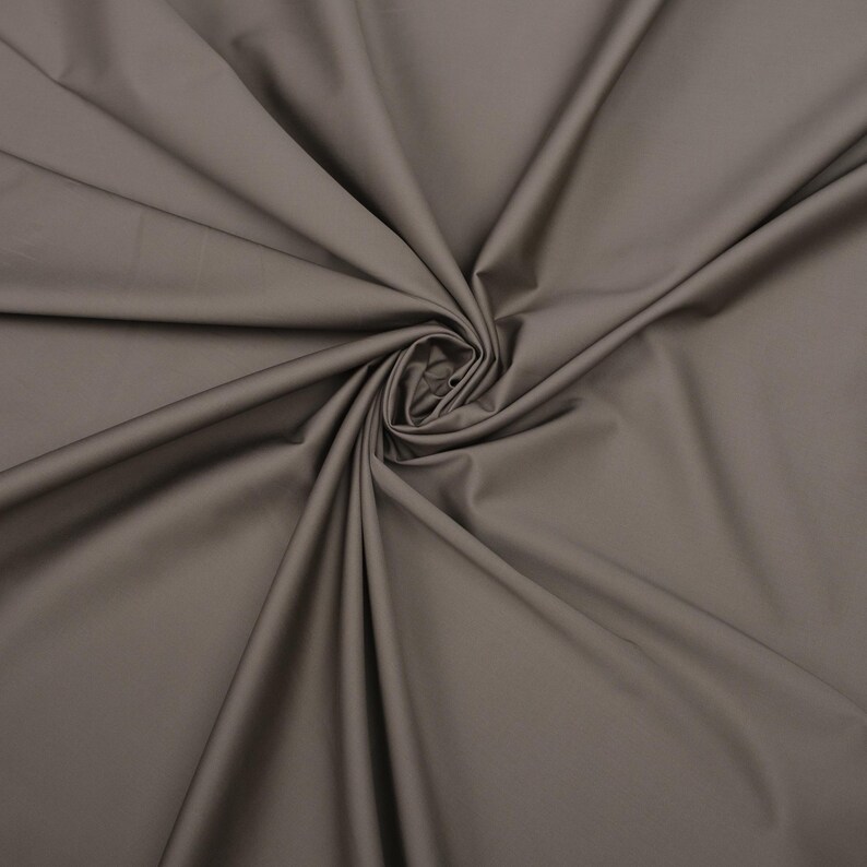 May include: A close-up of a smooth, gray fabric with a soft, drapey texture. The fabric is folded and arranged in a swirling pattern.