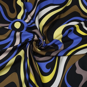Op de afbeelding: Close-up van een stof met een wervelend, abstract ontwerp. Het patroon heeft gebogen lijnen in zwart, blauw, geel, bruin en wit. De stof is waarschijnlijk zijde of een vergelijkbaar materiaal, met een lichte glans.