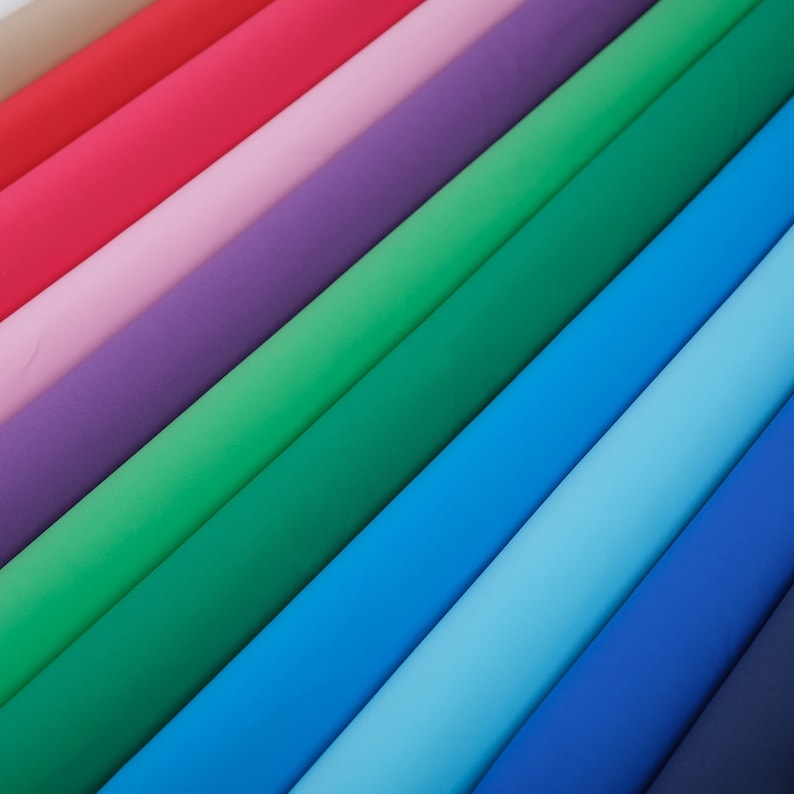 May include: A collection of fabric swatches in various colors, including beige, red, pink, purple, green, blue, light blue, and dark blue. The fabric swatches are arranged in a diagonal pattern, creating a rainbow effect.