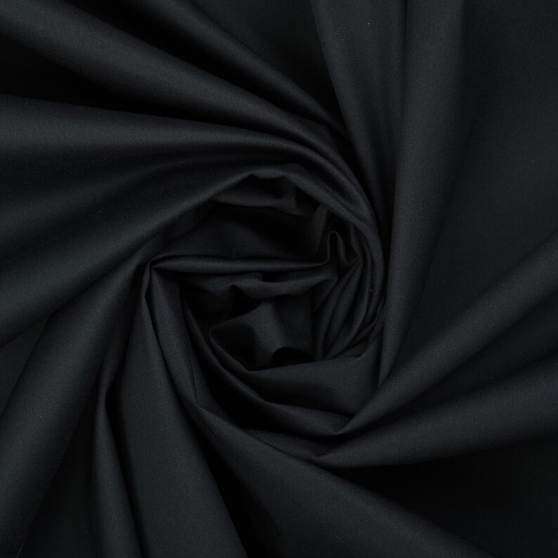 May include: Black fabric with a smooth, silky texture. The fabric is folded and draped, creating a soft, flowing look.