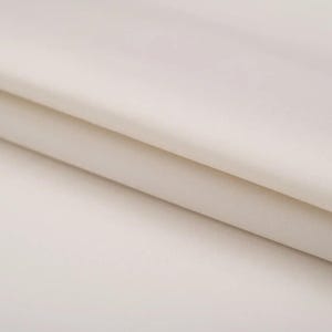 May include: Close-up of a smooth, off-white fabric with a subtle sheen. The fabric is folded in half, creating a soft, gentle curve.