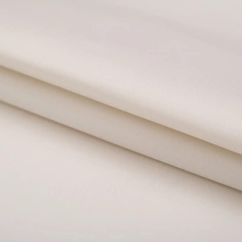 May include: Close-up of a smooth, off-white fabric with a subtle sheen. The fabric is folded in half, creating a soft, gentle curve.