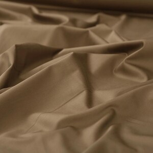 May include: A close-up of a smooth, brown fabric with soft folds and wrinkles. The fabric has a subtle sheen and a luxurious feel.