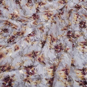 May include: White fabric with a floral pattern in shades of burgundy, yellow, and gold. The fabric has a subtle shimmer and a soft, flowing texture.