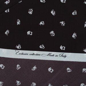 May include: Black fabric with a repeating pattern of white bunny illustrations. A light blue strip across the bottom features the text "Exclusive collection Made in Italy". The fabric has a dark brown border.