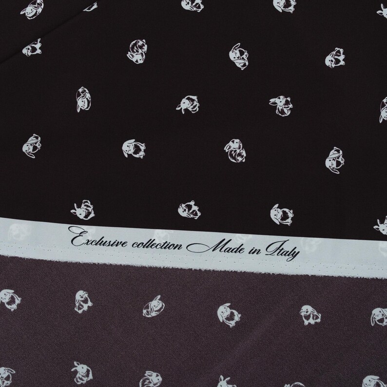 May include: Black fabric with a repeating pattern of white bunny illustrations. A light blue strip across the bottom features the text "Exclusive collection Made in Italy". The fabric has a dark brown border.