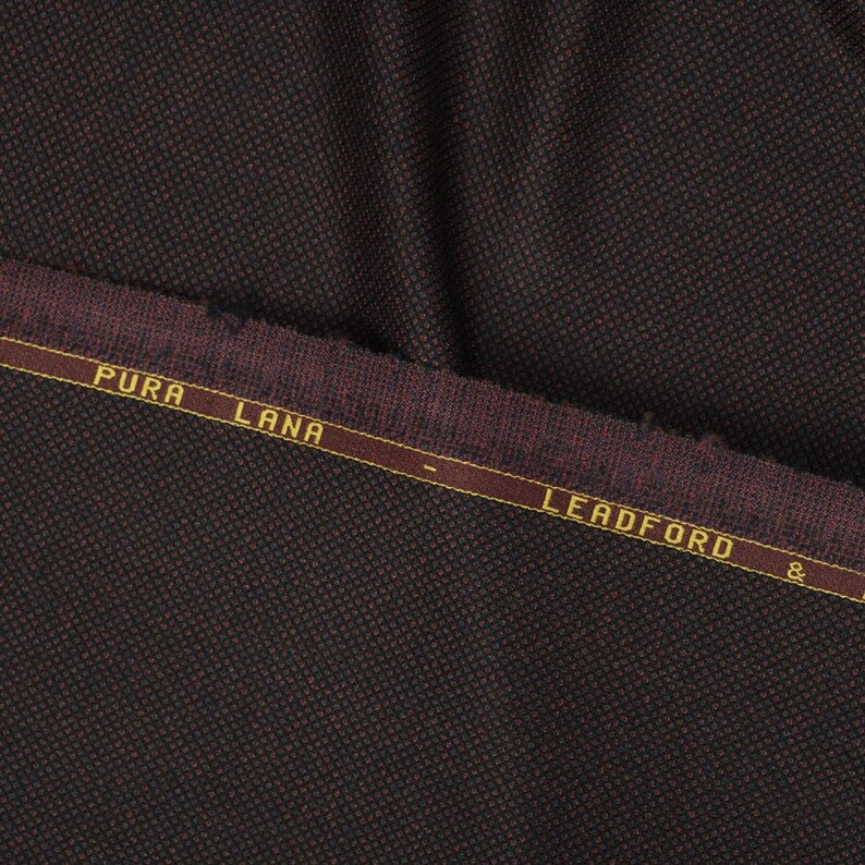 May include: Close-up of a dark brown fabric with a subtle textured pattern. The fabric has a burgundy colored border with the text "PURA LANA - LEADFORD &" in gold lettering.