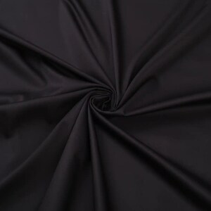 May include: Close-up of a smooth, black fabric with a soft, flowing texture. The fabric is draped and folded, creating a dramatic and elegant look.