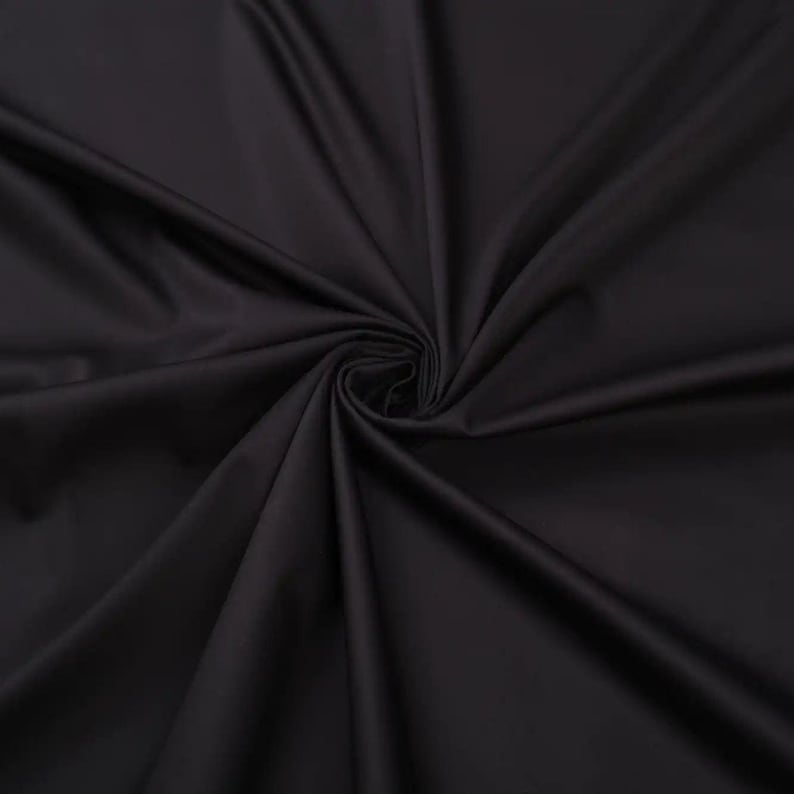 May include: Close-up of a smooth, black fabric with a soft, flowing texture. The fabric is draped and folded, creating a dramatic and elegant look.