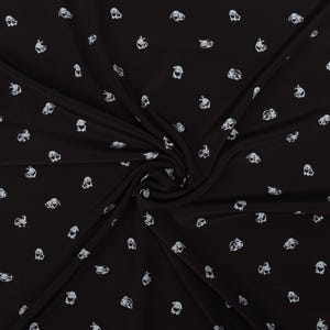 May include: Black fabric with a repeating pattern of white bunny illustrations. The bunnies are depicted in various poses and orientations, creating a playful and whimsical design. The fabric is draped, showing folds and shadows.