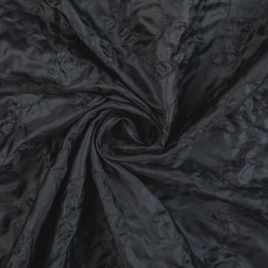 Könnte beinhalten: Nahaufnahme eines schwarzen, gesteppten Stoffes mit Rautenmuster. Der Stoff ist gewirbelt, wodurch Falten und Schatten entstehen, die seine Textur und seinen Glanz hervorheben. Das Material wirkt glatt und luxuriös, geeignet für verschiedene Nähprojekte.