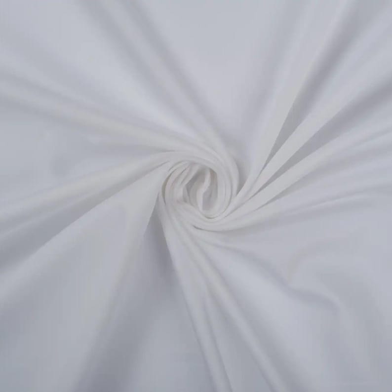 May include: White fabric with a smooth, silky texture. The fabric is folded and draped, creating soft folds and curves.