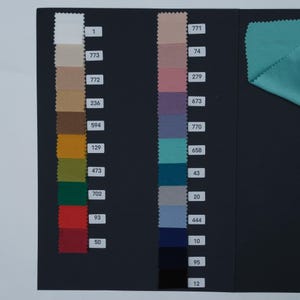 May include: A color swatch card featuring fabric samples in various colors, including white, beige, brown, yellow, green, red, teal, blue, and purple. Each color is labeled with a number. A piece of teal fabric is in the upper right corner.