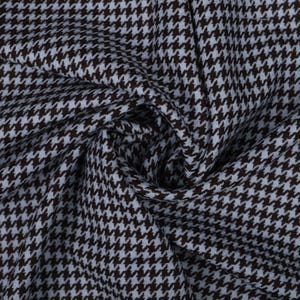 Op de afbeelding: Close-up van een stof met een hondenpoottandpatroon. De stof heeft een herhalend ontwerp van kleine, gebroken ruitjes in bruin en lichtblauw. Het materiaal is zacht en lijkt gedrapeerd te zijn, met zichtbare plooien en schaduwen.