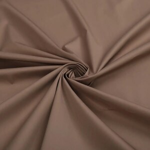 May include: A close-up of a smooth, brown fabric with a soft, drapey texture. The fabric is folded and arranged in a swirling pattern, highlighting its flexibility and drape.