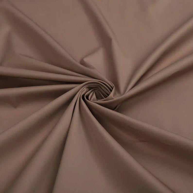 May include: A close-up of a smooth, brown fabric with a soft, drapey texture. The fabric is folded and arranged in a swirling pattern, highlighting its flexibility and drape.