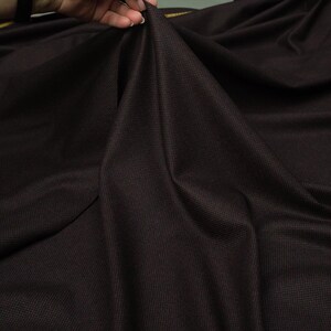 May include: A dark brown fabric with a subtle woven pattern. The fabric is smooth and has a slight sheen.