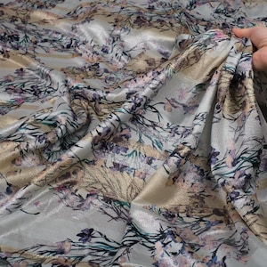 May include: Silver fabric with a floral print in shades of pink, blue, and gold. The fabric has a subtle shimmer and a soft, flowing texture.