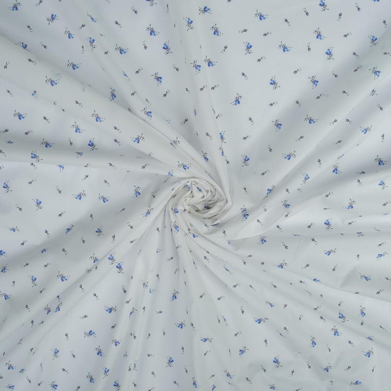 May include: White fabric with a delicate floral pattern. The fabric features small blue flowers and tiny gray leaves scattered across its surface. The fabric is gathered in a swirl, showcasing its texture and design.