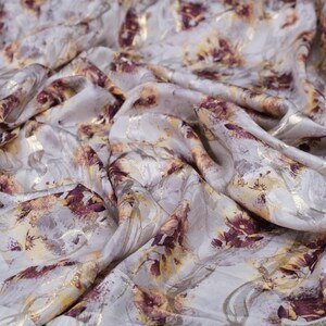May include: White fabric with a floral pattern in shades of gold and burgundy. The fabric has a subtle sheen and a soft, flowing texture.