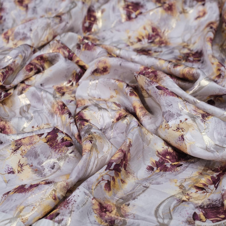 May include: White fabric with a floral pattern in shades of gold and burgundy. The fabric has a subtle sheen and a soft, flowing texture.