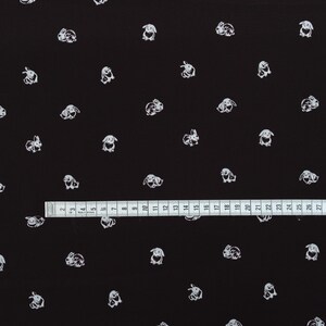 May include: Black fabric with a repeating pattern of white bunny illustrations. A ruler is placed across the bottom of the fabric, showing measurements in inches. The bunnies are in various poses.