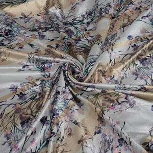 May include: A close-up of a silver fabric with a gold and purple floral pattern. The fabric is soft and has a subtle sheen.