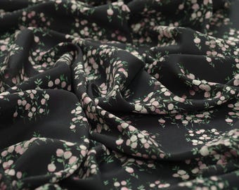 May include: Black fabric with a delicate white and pink floral pattern. The fabric is soft and flowing, making it ideal for creating garments or home decor.