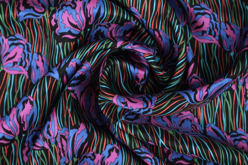 May include: Black fabric with a colourful floral pattern. The fabric features pink, blue and green flowers on a black background with thin, colourful stripes.
