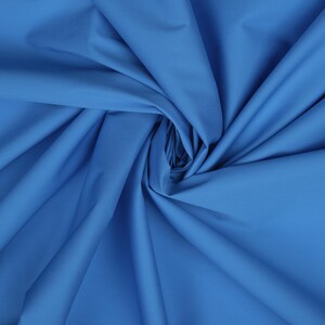 May include: A close-up of a smooth, blue fabric with a soft, flowing texture. The fabric is folded and draped, creating a sense of movement and depth.