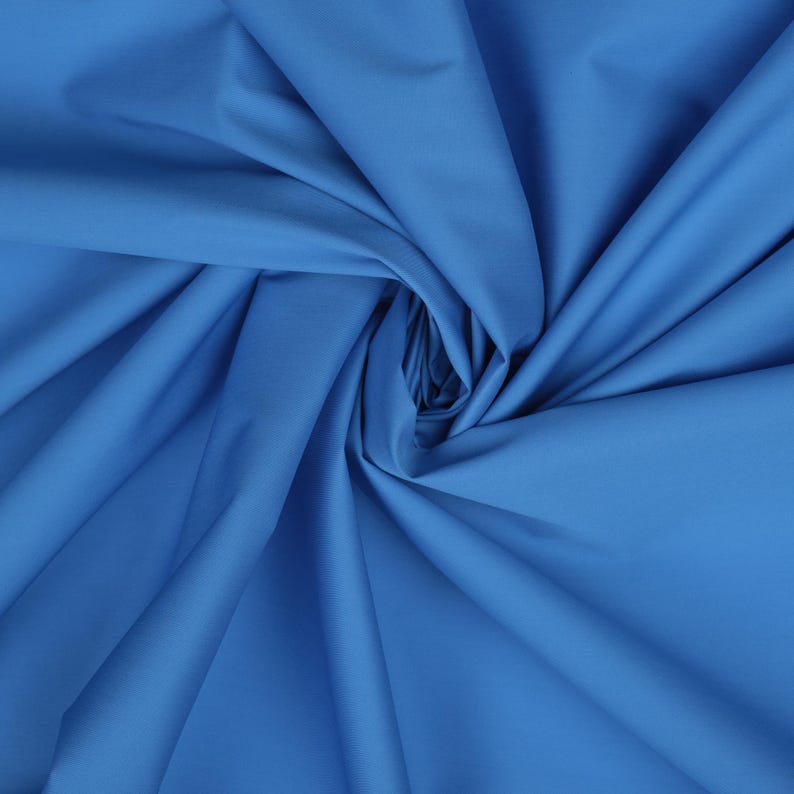 May include: A close-up of a smooth, blue fabric with a soft, flowing texture. The fabric is folded and draped, creating a sense of movement and depth.
