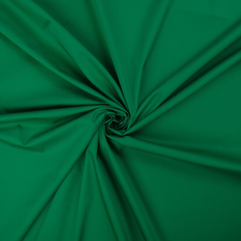 May include: A close-up of a deep green fabric with a smooth texture. The fabric is folded and draped, creating a soft, flowing look.