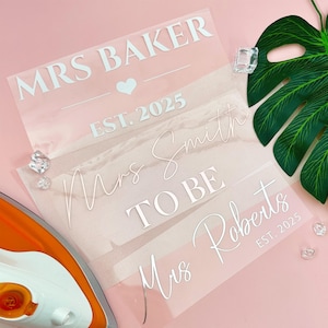 May include: Three heat transfer vinyl sheets for wedding crafts. The top sheet reads "MRS BAKER" with a heart and "EST. 2025". The second sheet says "Mrs Smith TO BE". The bottom sheet says "Mrs Roberts EST. 2025".