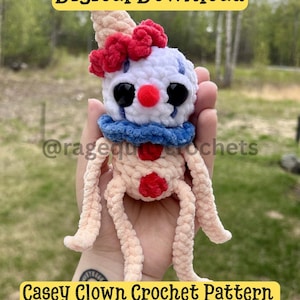 May include: A crochet clown doll with a white head, red nose, large black eyes, and blue collar. It features a red pom-pom on the head and two red buttons on the body. The text reads Digital Download and Casey Clown Crochet Pattern.