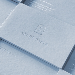 以下が含まれることがあります： 薄い青色の名刺が積み重ねられており、名刺には「AZURE PAPER」という文字と、窓枠の中に三日月と波のロゴが描かれている。名刺には「KATE JUN Director」という文字も書かれている。