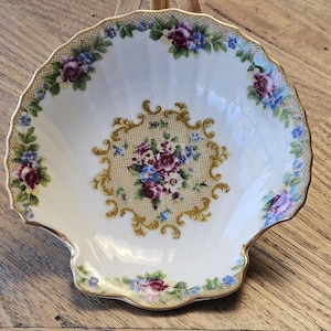May include: A shell-shaped dish with a cream-coloured base, gold trim, and floral patterns. The dish has a central floral bouquet in shades of purple, blue, and pink, set against a gold lattice. Floral arrangements also decorate the rim, giving a vintage feel.