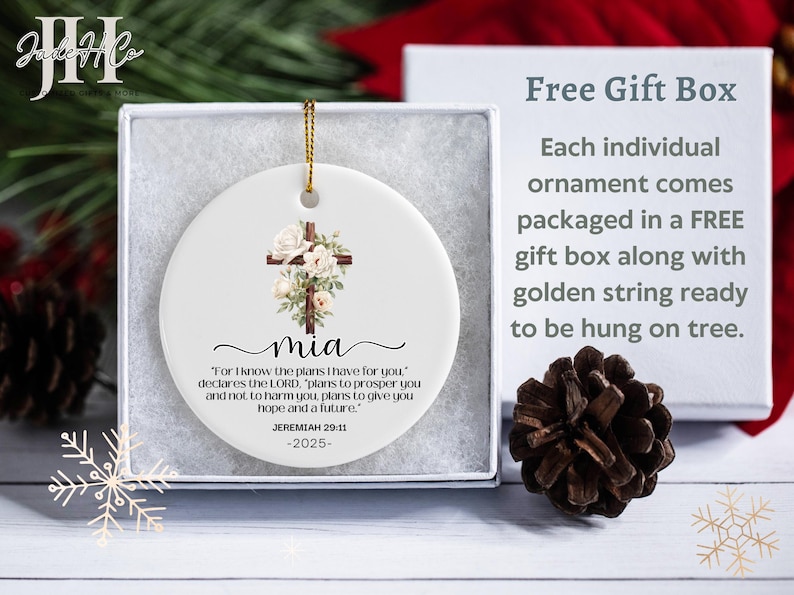 May include: White ceramic Christmas ornament with a floral cross design and the name "mia". The ornament includes a gold string for hanging and is packaged in a gift box. The text "For I know the plans I have for you" is also included.