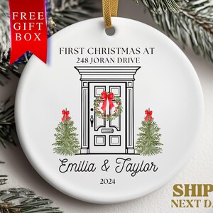 May include: White ceramic Christmas ornament with a black and white illustration of a house with a wreath on the door. The text "FIRST CHRISTMAS AT 248 JORAN DRIVE Emilia & Taylor 2024" is printed on the ornament.