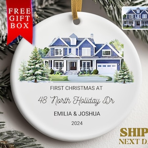 May include: A white ceramic Christmas ornament with a watercolor illustration of a blue house with white trim. The text "FIRST CHRISTMAS AT 48 North Holiday Dr EMILIA & JOSHUA 2024" is printed on the ornament.