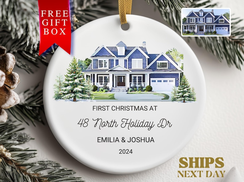 May include: A white ceramic Christmas ornament with a watercolor illustration of a blue house with white trim. The text "FIRST CHRISTMAS AT 48 North Holiday Dr EMILIA & JOSHUA 2024" is printed on the ornament.