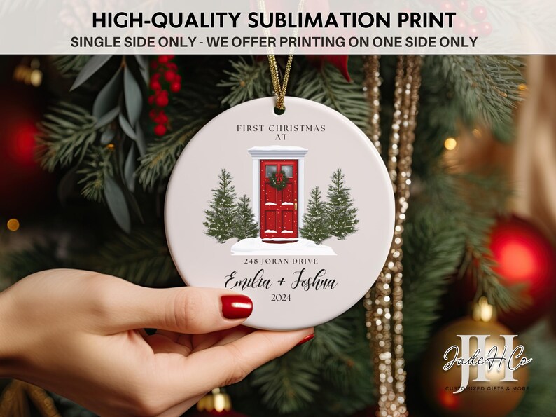 May include: White ceramic Christmas ornament with a red door, two pine trees, and the text "First Christmas at 248 Joran Drive Emilia + Joshna 2024".