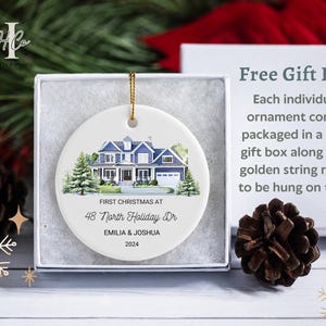 May include: White ceramic Christmas ornament with a watercolor painting of a blue house. The ornament reads "First Christmas at 48 North Holiday Dr. Emilia & Joshua 2024".