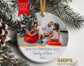 May include: Round Christmas ornament featuring a family photo. The ornament has the text "OUR 1ST CHRISTMAS AS A Family of Four 2025". A red ribbon with "FREE GIFT BOX" is attached. The ornament is hanging with a gold ribbon.