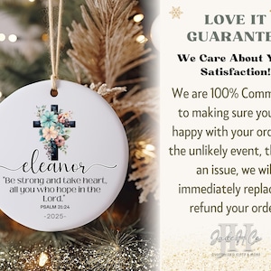 May include: A white ceramic Christmas ornament with a floral cross design and the name "eleanor". The ornament includes the text "Be strong and take heart, all you who hope in the Lord." Psalm 31:24 -2025-.
