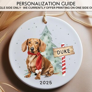 May include: A round Christmas ornament featuring a dachshund wearing a red scarf, a Christmas tree, and a sign that says "DUKE". The year "2025" is printed at the bottom. The text "PERSONALIZATION GUIDE" is at the top.
