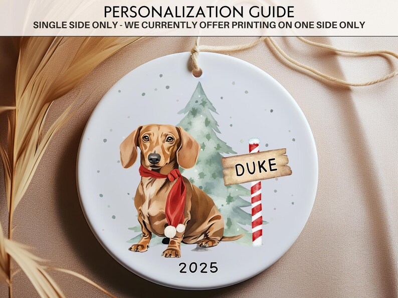 May include: A round Christmas ornament featuring a dachshund wearing a red scarf, a Christmas tree, and a sign that says "DUKE". The year "2025" is printed at the bottom. The text "PERSONALIZATION GUIDE" is at the top.