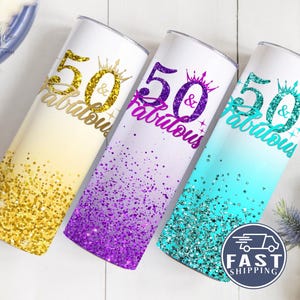May include: Three 20 oz. stainless steel tumblers with a glitter ombre design. The tumblers are decorated with the text "50 & Fabulous" in gold, purple, and turquoise glitter.